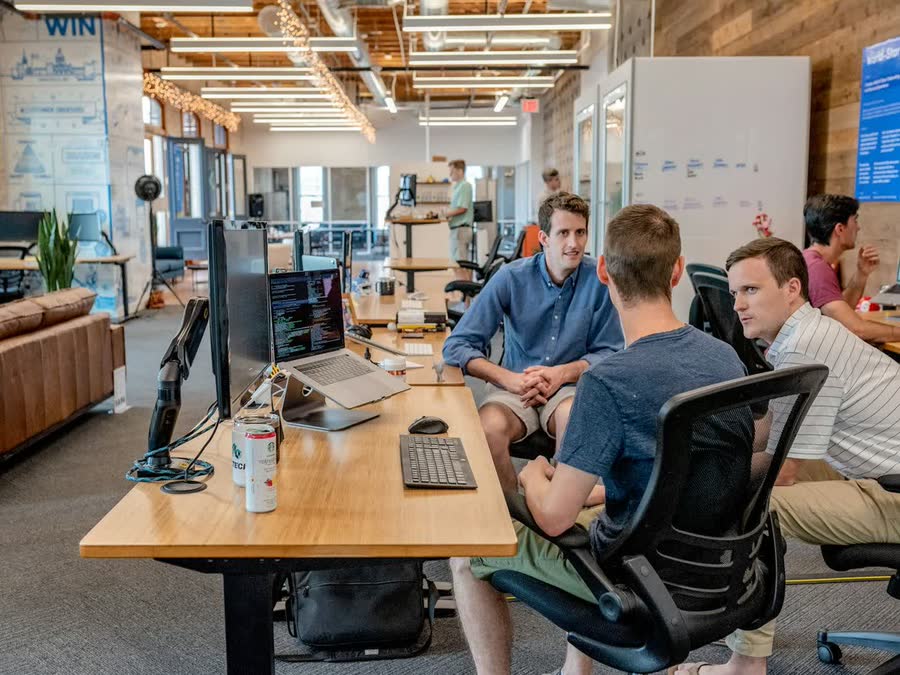 Three colleagues talking at a desk in an open-plan office